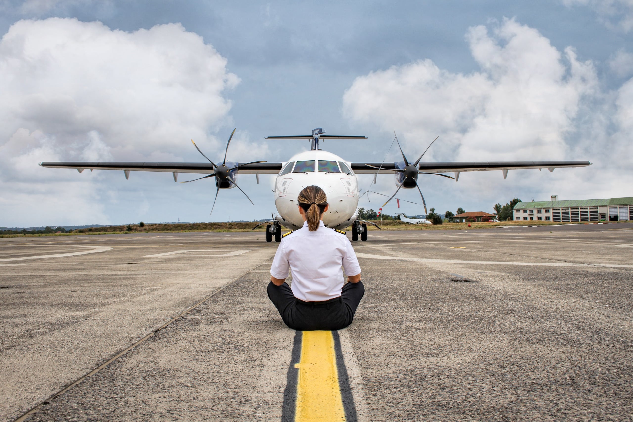 femme pilote assise en tailleur devant un avion sur le tarmac